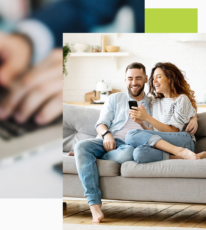 Happy couple on couch smiling as female shows male her phone and financial blog tips